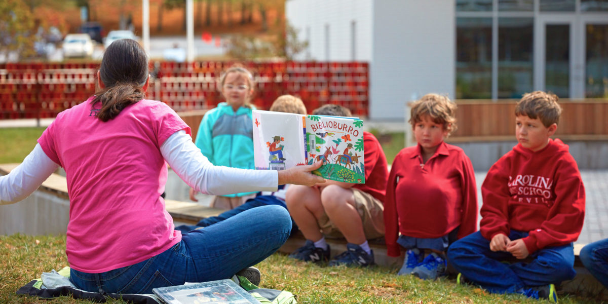 A teacher reads to K-12 students outdoors. Photo by Mark Herboth Photography.